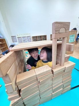 兩位幼兒將積木堆砌成城堡，並躲在城堡中央